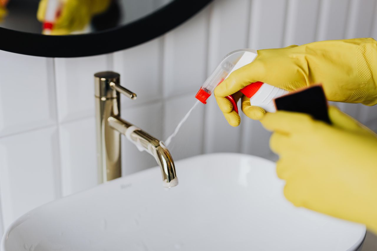 services-02 Vue d'en haut d'une femme de ménage anonyme portant des gants en caoutchouc jaunes et pulvérisant un nettoyant vers un robinet chromé dans une salle de bain
